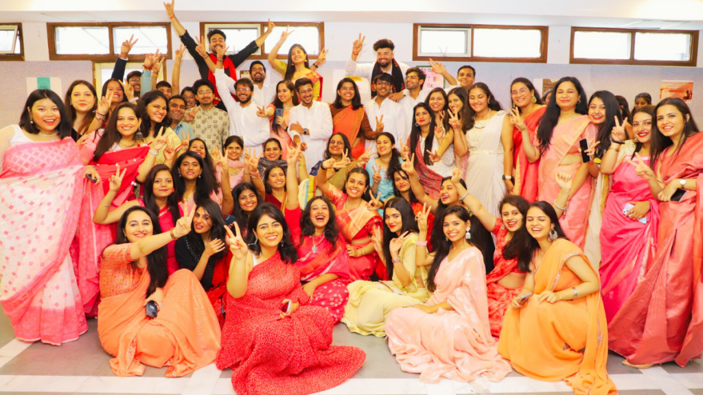 A large group of cheerful people dressed in colorful attire posing for a group photo in an indoor setting.